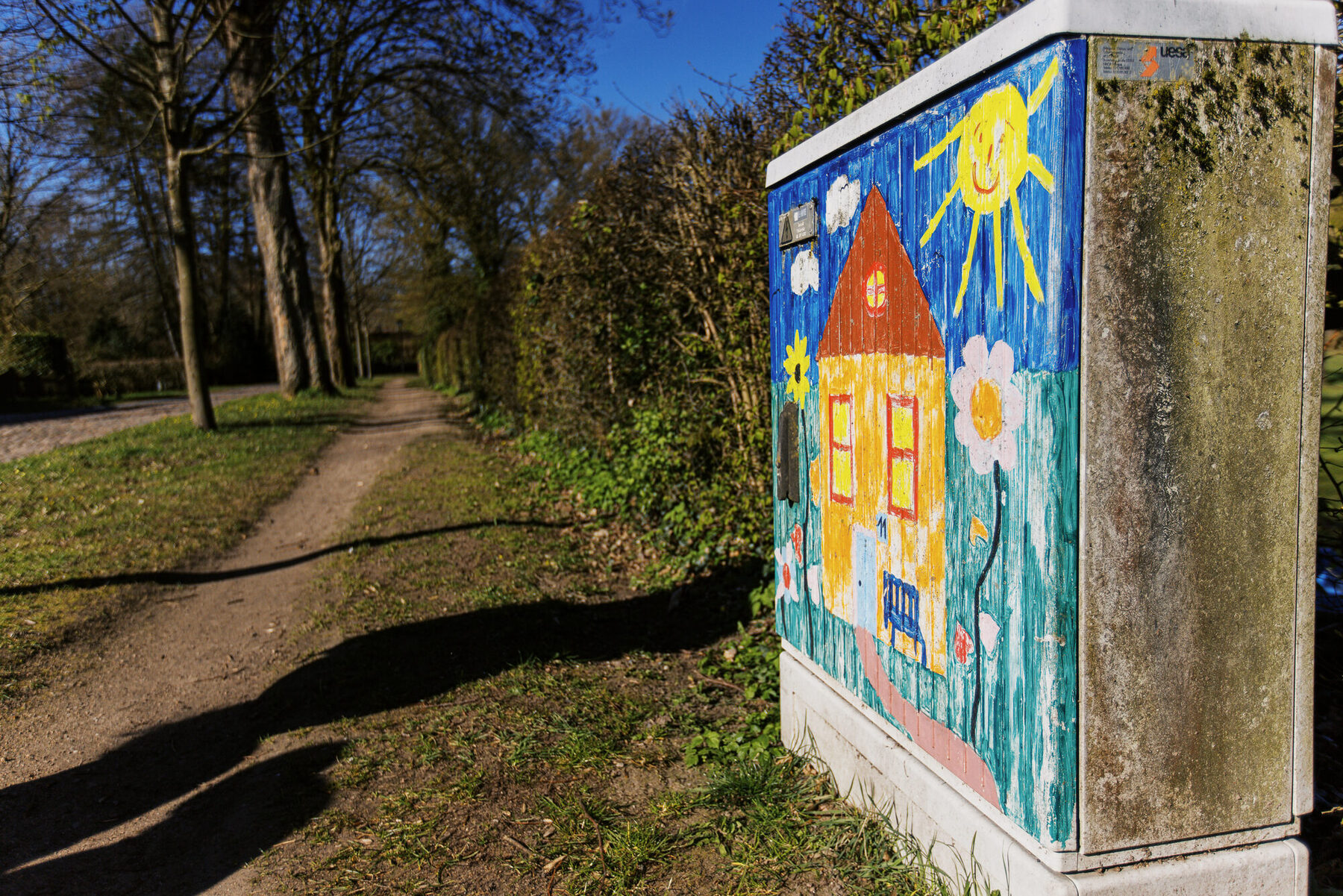 Bunt bemalter Kasten mit Hausmotiv an einem Weg in Tostedt