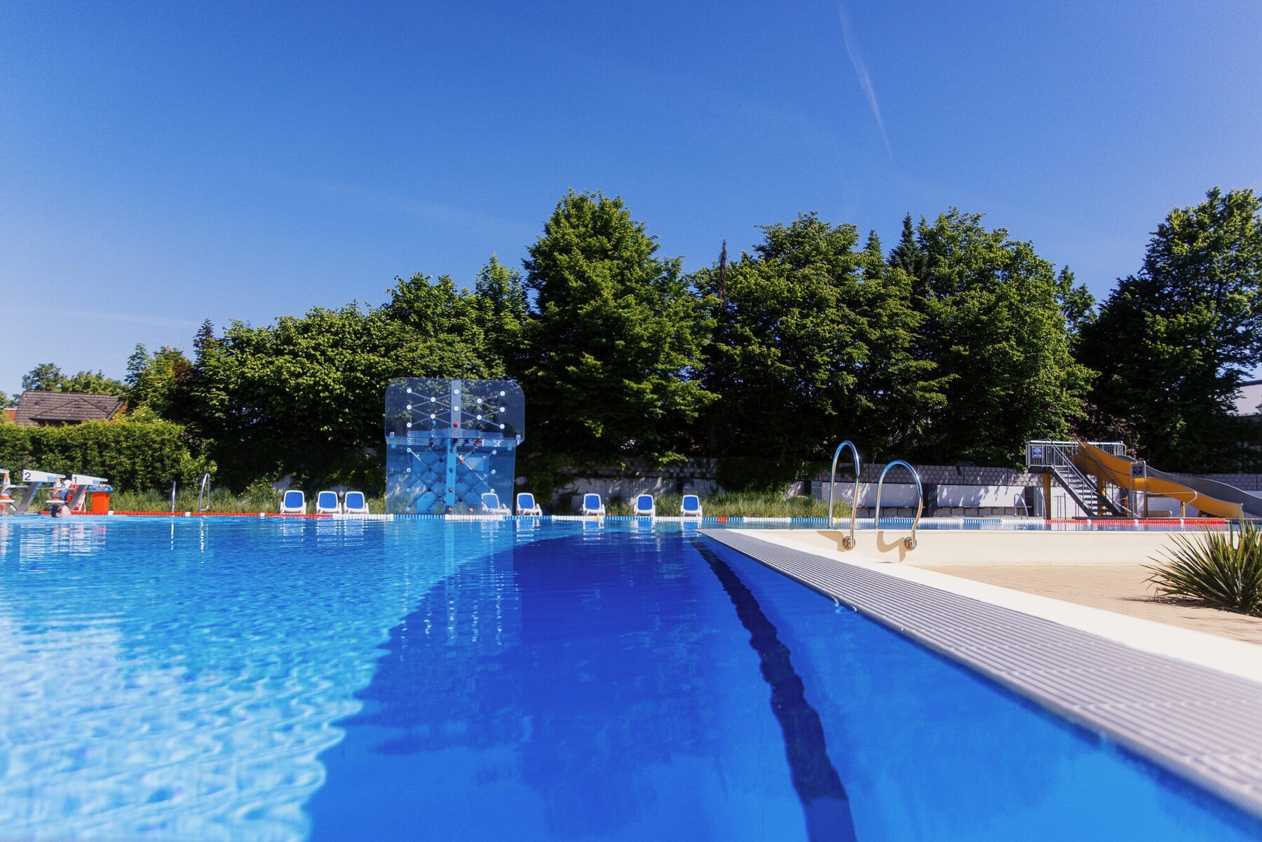 Blaues Schwimmbecken des Freibads Tostedt mit Bäumen im Hintergrund